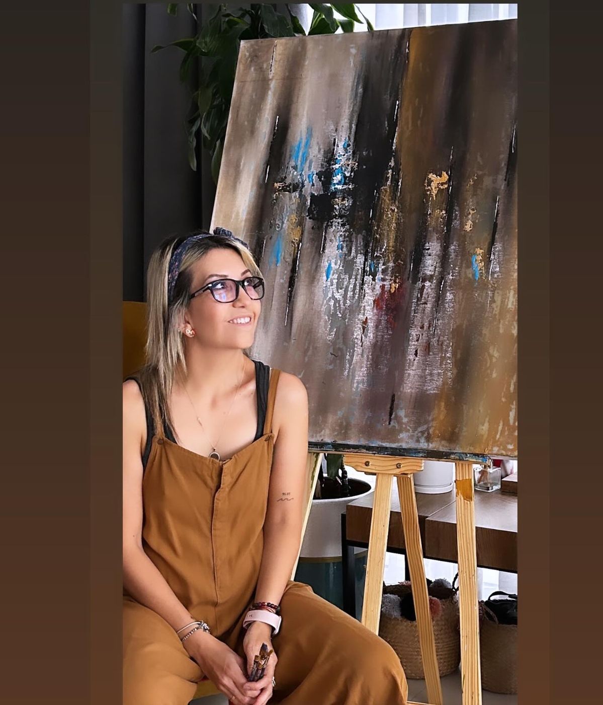 Özlem Çuhadar seated beside one of her paintings